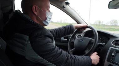 Koruyucu tıbbi maskeli bir adam kontak anahtarını çevirir ve sürmeye başlar. Koronavirüs salgınından korunmak için karantina sırasında güvenli bir taksi yolculuğu. Rusya, Volgodonsk: 16 Nisan 2020.