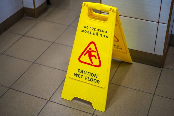 Warning sign with Russian text caution wet floor. Sign in the corridor of the office or entertainment center. Cleaning ceramic tiles in the toilet. Copy space