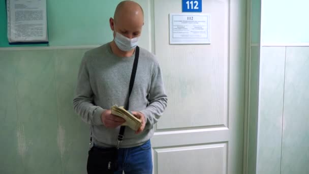 医療マスクの男が事務所のドアの下の病院の廊下の列に立って医者の予約を待っている ロシア ヴォルゴンドンスク2020年4月23日 — ストック動画