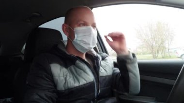 Araba kullanan bir adam koruyucu bir tıbbi maskeyi çıkarır. Koronavirüs salgını sırasında güvenli bir taksi yolculuğu. Karantinanın sonu. Sürücü ve yolcuları bakteriyel ve viral enfeksiyonlardan koru.