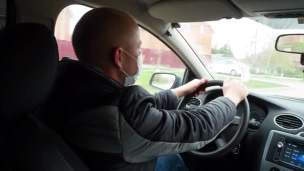 En man som kör bil i en skyddande medicinsk mask vrider på tändnyckeln och börjar köra. Säker taxiresa under karantänen från coronaviruspandemin. Ryssland, Volgodonsk: 16 april 2020. — Stockvideo