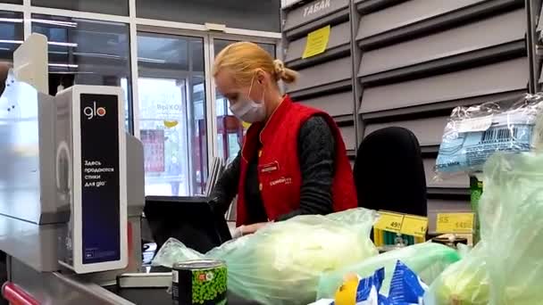 Een vrouw kassier in beschermende masker en handschoenen verkoopt voedsel in de supermarkt bij de kassa. Bescherming van de verkoper en kopers tijdens het quarantaine- en pandemische coronavirus. Rusland, Volgodonsk: 10 mei 2020. — Stockvideo