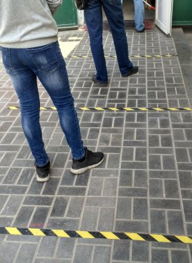 Caddede bir dükkan için kuyruğa gir. Sosyal mesafe. İnsanların ayakları yiyecek almak için güvenli bir şekilde mağazaya girmeyi bekliyor. Koronavirüs salgını sırasında birbirinden uzak olmak için çizgilerin güvenli bir şekilde işaretlenmesi. Dikey.