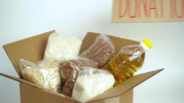 Karton bağış kutusunda yiyecek, beyaz arka planda izole edilmiş. Karantina süresi için gerekli malların kriz önleyici stoku. Yemek teslimatı, koronavirüs. Yiyecek kıtlığı. Metinle imzala.