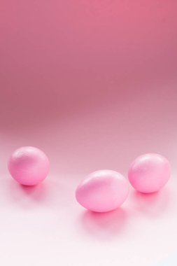 Pembe bir arka planda gelişigüzel duran üç pembe yumurta. Tek Renkli