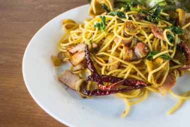 Pastırma ve ahşap arka plan üzerinde beyaz tabak içinde fesleğen ile baharatlı spagetti