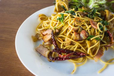 Pastırma ve ahşap arka plan üzerinde beyaz tabak içinde fesleğen ile baharatlı spagetti