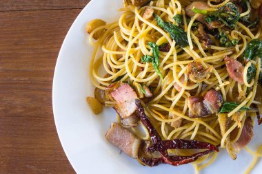 Pastırma ve ahşap arka plan üzerinde beyaz tabak içinde fesleğen ile baharatlı spagetti