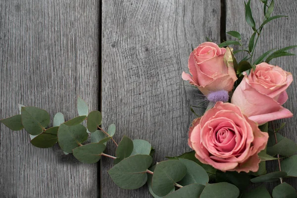 Kırsal bir arka planda üç pembe gül. Gri ahşap arka planda güller