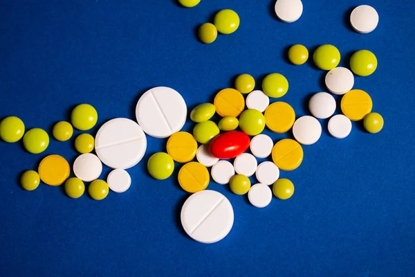 Sarı, beyaz, yeşil haplar ve mavi arka planda bir kırmızı kapsül.