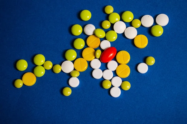 Sarı, beyaz, yeşil haplar ve mavi arka planda bir kırmızı kapsül.
