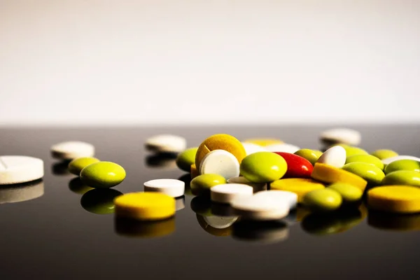 Sarı, beyaz, yeşil haplar ve siyah beyaz arka planda bir kırmızı kapsül.