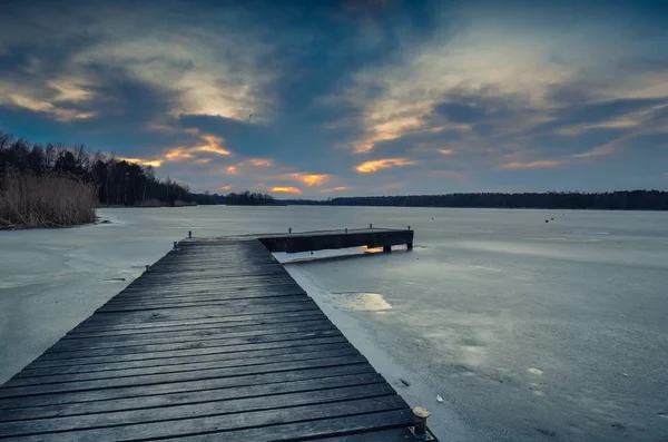 Evening winter landscape. Wooden pier over a beautiful frozen lake.