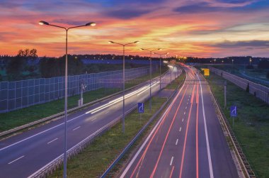 Geceleri otoban. Polonya 'da A1 karayolu üzerinde ışık saçan güzel renkli gökyüzü.
