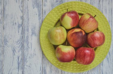 Taze kırmızı meyveler. Ahşap bir arka planda yeşil bir tabakta elmalar.