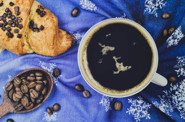 Interesting winter concept for serving coffee. Black coffee with croissants on a blue background with snowflakes.