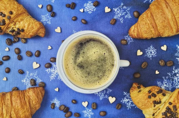 Interesting idea for serving coffee with a sweet snack. Coffee with marshmallows and croissants on a blue winter background.