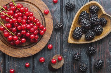 Mutfakta kırmızı ve siyah meyve var. Kahverengi ahşap bir masada kırmızı frenk üzümü ve böğürtlen..