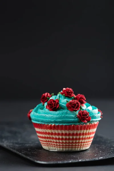 Blauwe cupcake met nep rode rozen op zwarte achtergrond — Stockfoto