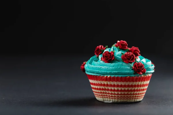 Cupcake bleu avec de fausses roses rouges sur fond noir — Photo