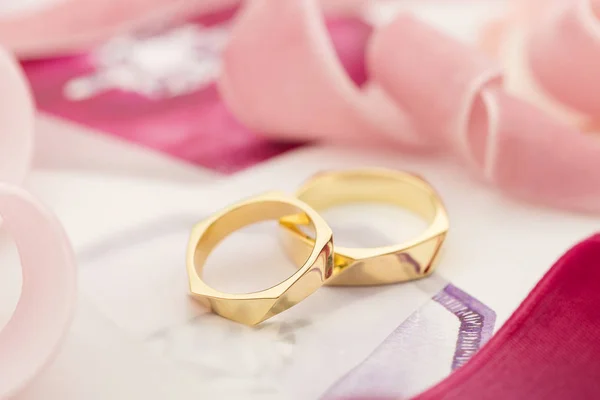 Golden wedding rings on pastel background with pink ribbons