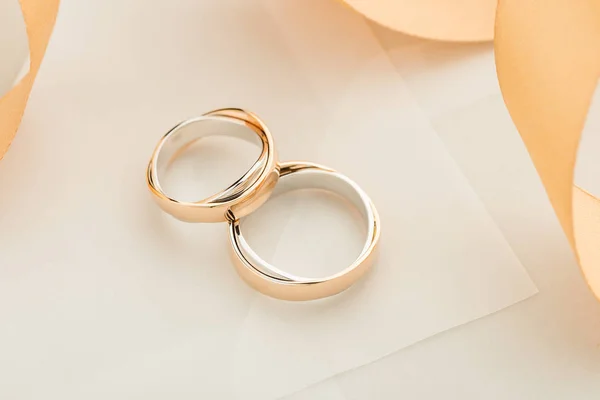 Two white and rose gold wedding rings on pastel background