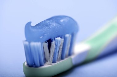 Diş fırçasını mavi bulanık arkaplanda mavi diş macunuyla kaplayın.