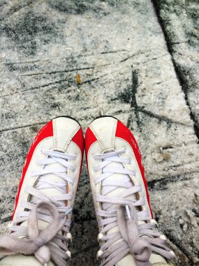 A pair of feet in women's skate lace-up boots, in white and red, close-up, against the scratched ice.  The view from the top. clipart