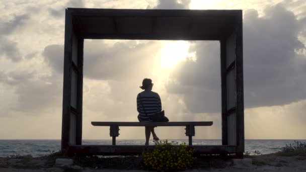 Ragazza su una panchina in riva al mare al tramonto — Video Stock