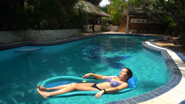 Jeune femme couchée sur un matelas d'eau dans la piscine par une journée ensoleillée — Video