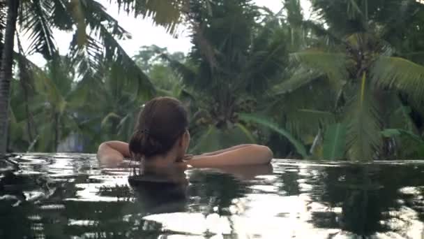 Junge Frau erholt sich im Pool im tropischen Garten — Stockvideo