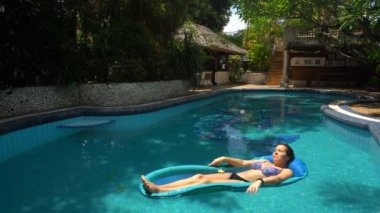 Genç bir kadın güneşli bir günde havuzda su yatağında yatıyor.