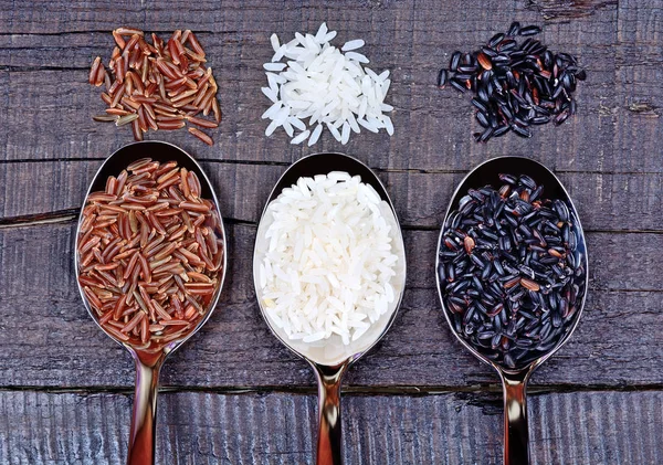 Lžíce s různými druhy rýže na stole — Stock fotografie
