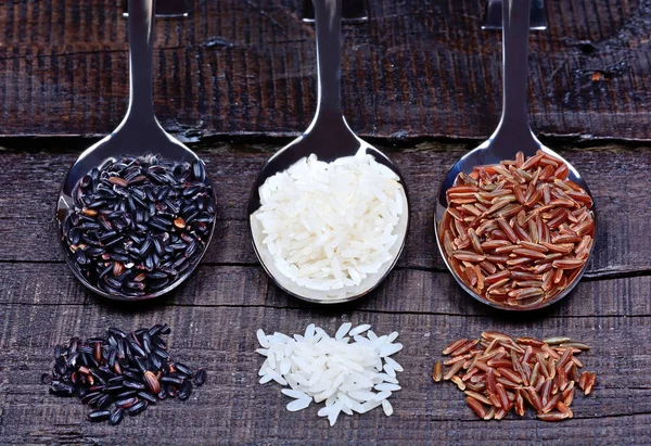 Různé typy rýže v lžíce na stole — Stock fotografie