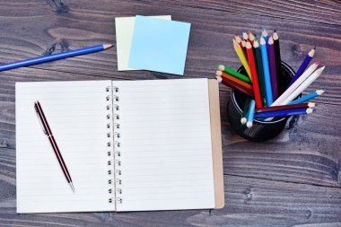 Boş defter ile kalem ve masada renkli kalemler