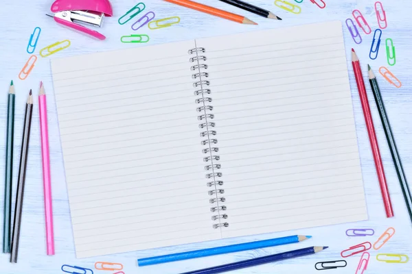 Bloco de notas com lápis coloridos, grampeador e clipes na mesa — Fotografia de Stock