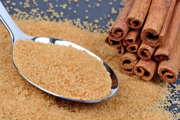 Brown sugar in a spoon with sticks of cinnamon