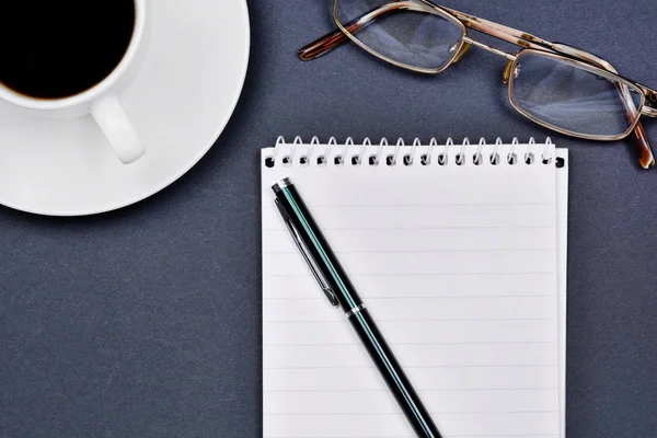 Schreibtisch mit offenem Notizblock, Stift, Brille und Kaffeetasse — Stockfoto