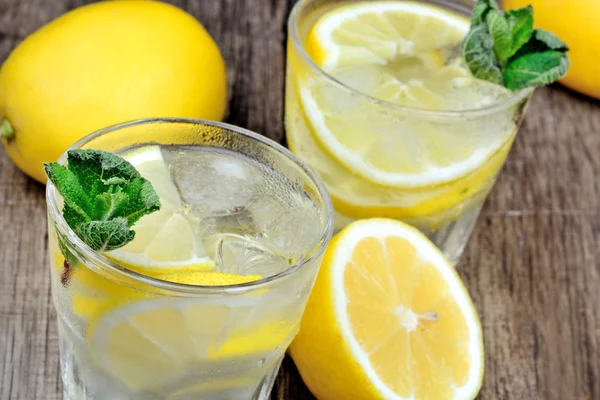 Gläser mit frischem Wasser mit Zitrone und Minze auf Holztisch — Stockfoto