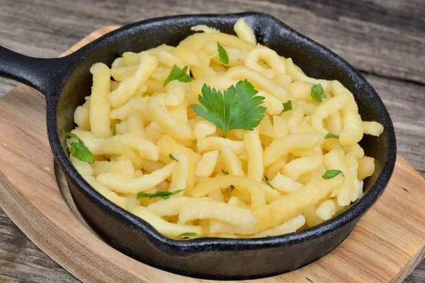 Spaetzle au beurre et persil dans une casserole en fer de planche à découper en bambou — Photo