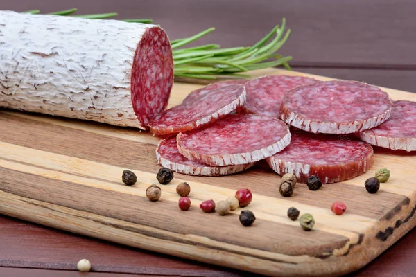 Salame com pimenta colorida e alecrim na tábua de corte — Fotografia de Stock