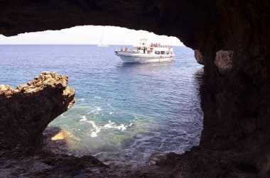 Sea view from the cave near the church on Cape Cavo Greco. Island Cyprus, Mediterranean Sea. Ship with tourists on a boat trip