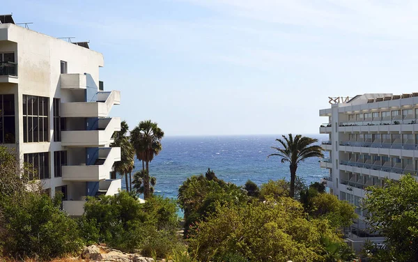 Beautiful seascape: clear blue sky, azure sea, waves, many green trees and shrubs, palm trees, hotels for vacationers. Cyprus island