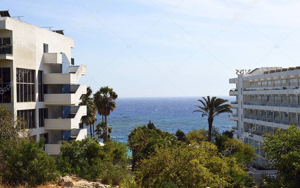Beautiful seascape: clear blue sky, azure sea, waves, many green trees and shrubs, palm trees, hotels for vacationers. Cyprus island