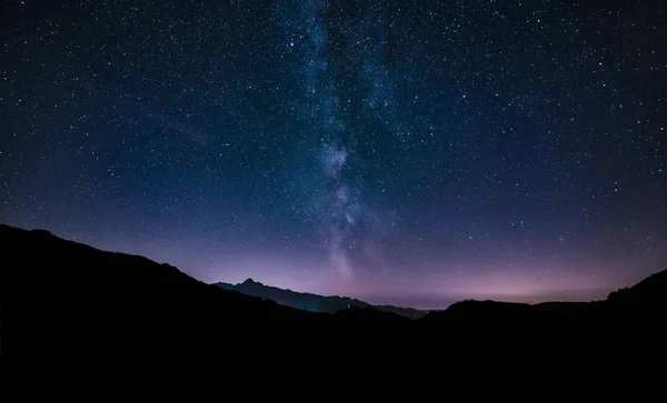 Estrellas del cielo púrpura noche. Vía Láctea galaxia a través de montañas . — Foto de Stock