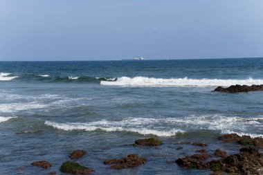 Mavi gökyüzünün altında gelgit dalgaları ve taşlarla dolu bir deniz..