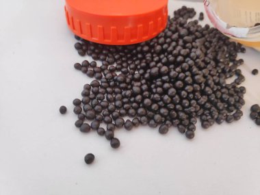 Ayurvedik siyah haplar beyaz arka planda ilaç şişesinden dökülüyor.