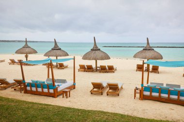 Dinlenme yerleri ve şemsiyeleri olan tropik tatil köyü plajı.