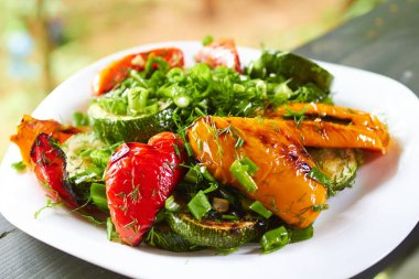 Izgara tatlı biber, kabak, yeşil soğan ve bitkilerle dolu bir yemek.