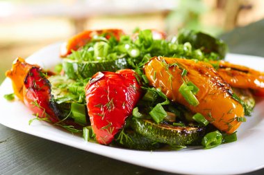 Izgara tatlı biber, kabak, yeşil soğan ve bitkilerle dolu bir yemek.